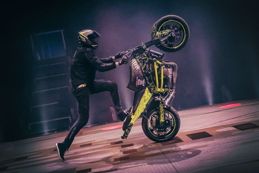 Ein Mann führt auf einer Bühne einen Motorradtrick vor.